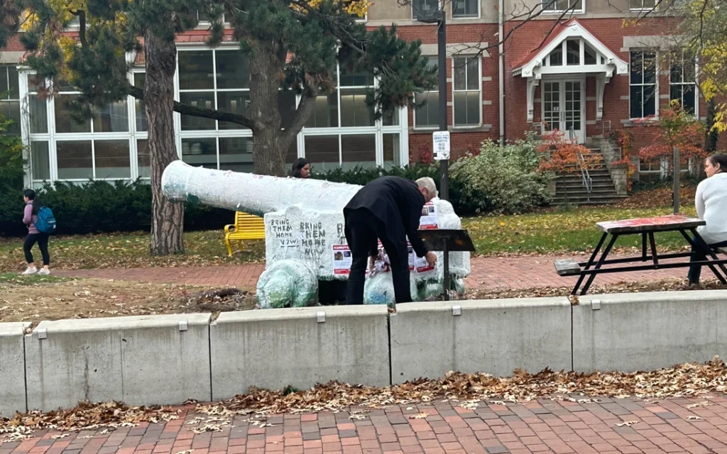 University of Guelph staff removes posters from the cannon statue on the University of Guelph campus while others walk nearby.