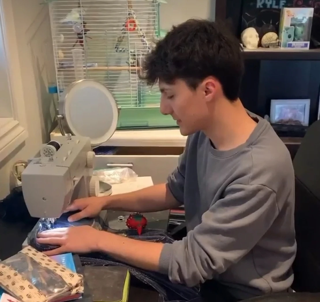A person operates a sewing machine at a desk with fabric and sewing tools.
