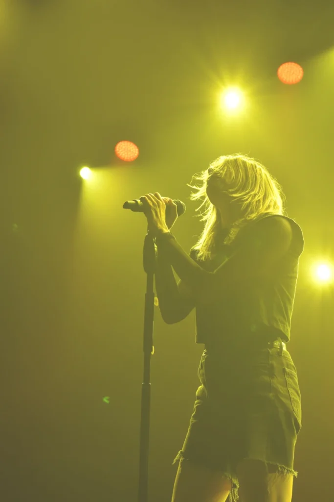 Singer performs into a microphone under yellow stage lighting.