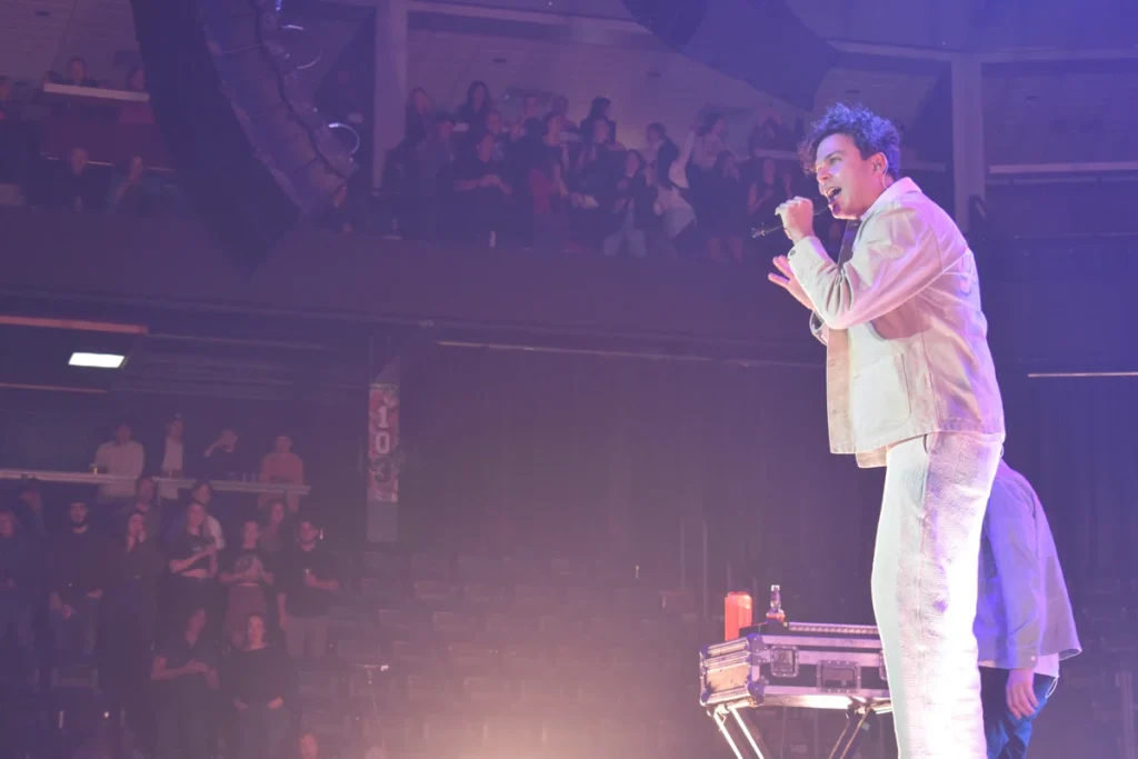 Musician sings into a microphone while performing onstage in front of an audience.