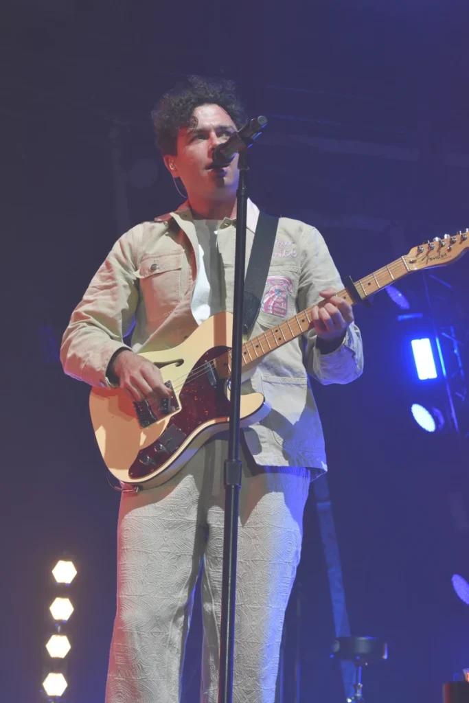 Arkells lead singer plays electric guitar and sings into a microphone under blue stage lighting.