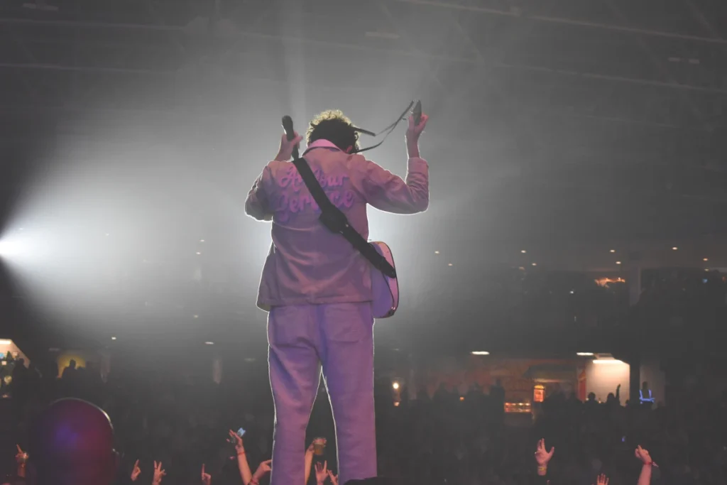 Arkells frontman stands facing the audience with arms raised while performing onstage.