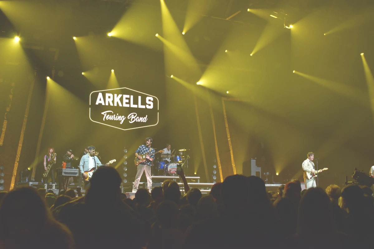 Arkells band performs onstage under yellow stage lights in front of a large audience.