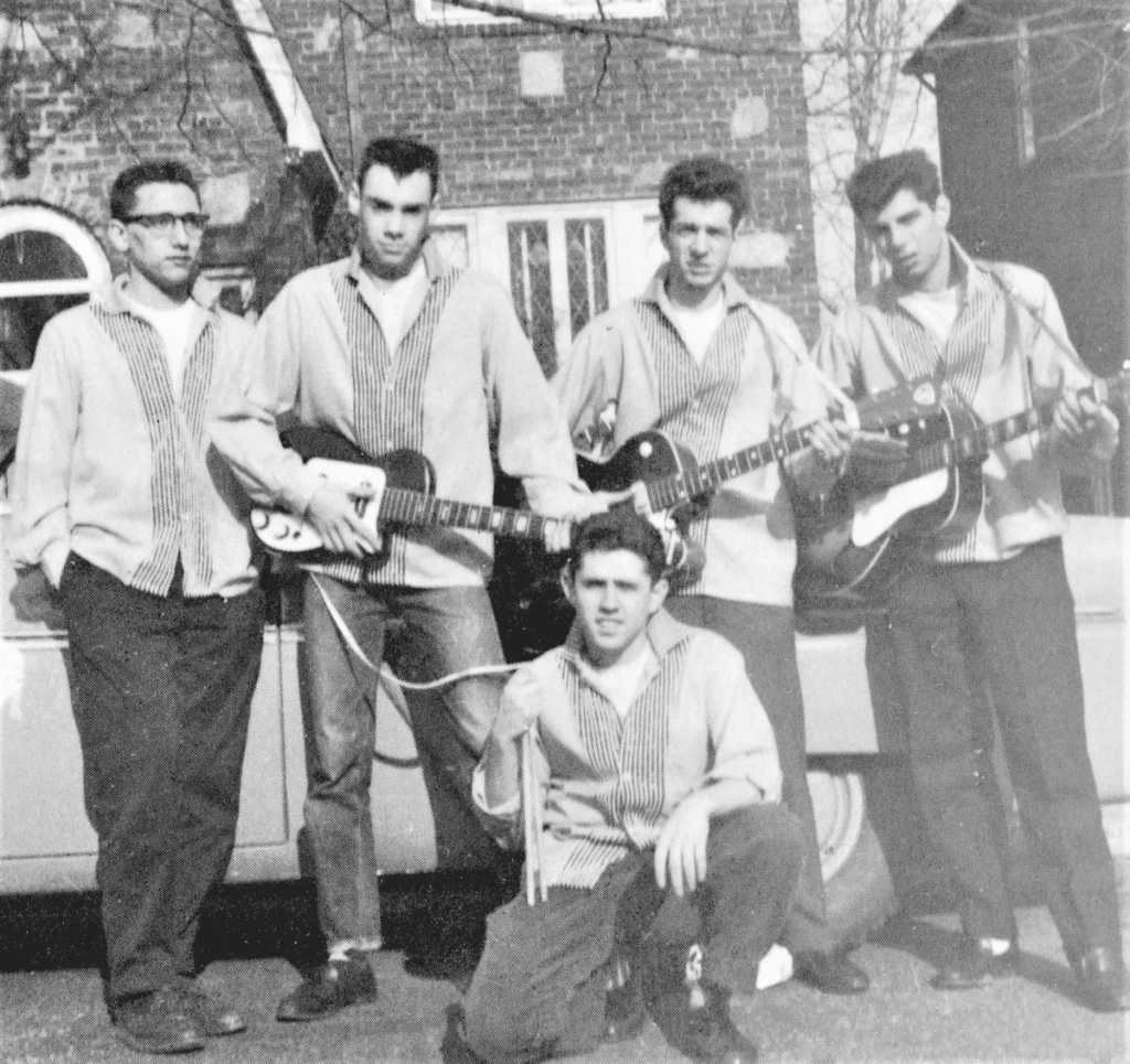Vintage black-and-white photo of a 1950s rock band posing with guitars beside a car.