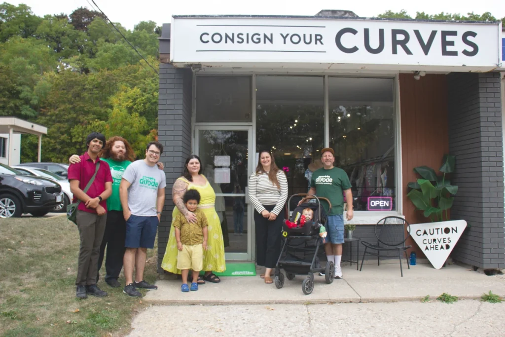 Group of people stand outside a storefront reading “Consign Your Curves".