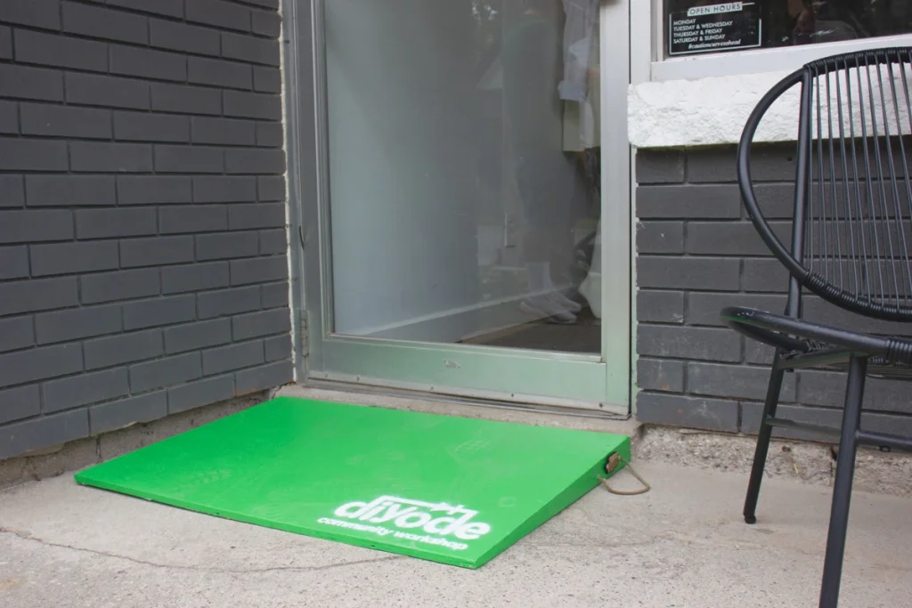 Bright green accessibility ramp labeled “diyode community workshop” placed at a storefront entrance.