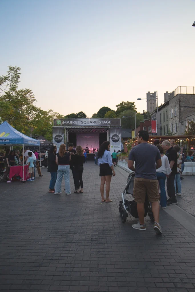 Crowd gathers along a pedestrian street facing the Market Square Stage during a Guelph Jazz Festival event.