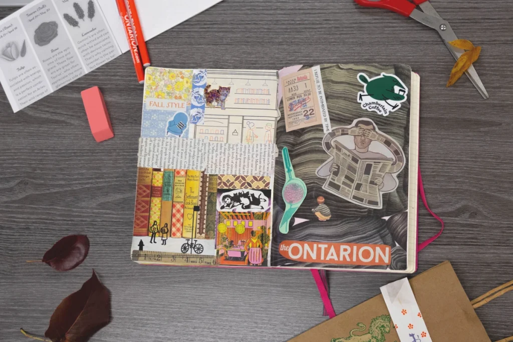 Open notebook decorated with collaged stickers, drawings, and a ticket stub on a desk with craft supplies.