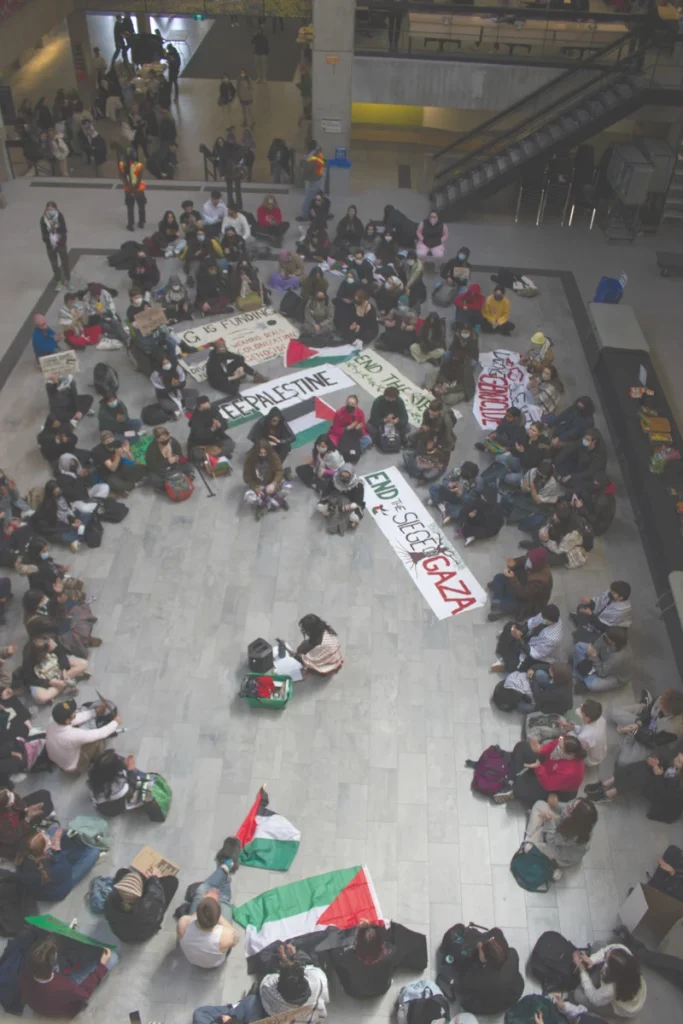 Students seated in the University Centre Courtyard holding banners reading “Free Palestine” and “End the Siege on Gaza.”