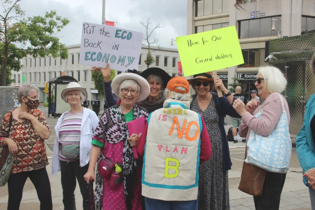 Seniors holding climate action signs reading “Put the ECO back in ECONOMY” and “There is No Plan B.”