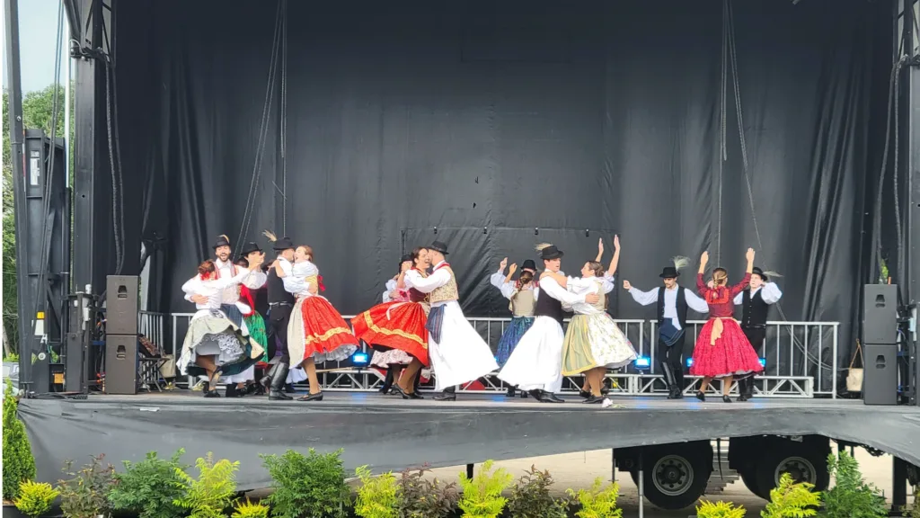 Performers in traditional folk costumes dance in pairs on an outdoor festival stage.